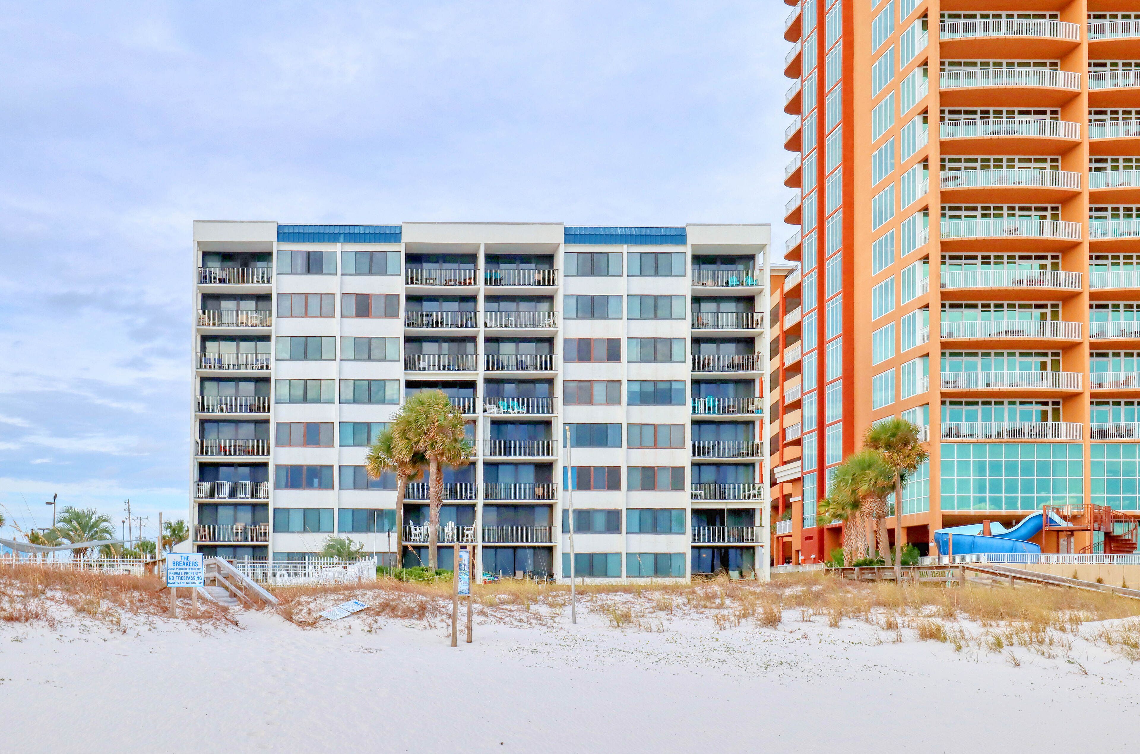 A multi-story hotel with balconies, a beach view, and a palm tree.