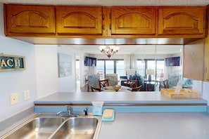 Une cuisine avec des meubles en bois, un évier à deux bacs et une vue sur le salon.