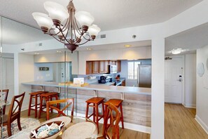 A modern kitchen with a central island, wooden chairs, and a chandelier.