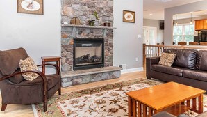 A living room with a stone fireplace, a brown leather sofa, a wooden coffee table, and a patterned rug. - SLOPESVIEW 4,400sq ft ~ 3 Level Home~ 6 BR,4BA, Sleeps 16~ Games!Walk to slopes! (Lake Harmony)