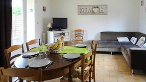 Zona pranzo con tavolo rotondo apparecchiato per quattro persone, televisore su supporto e divano grigio sullo sfondo.