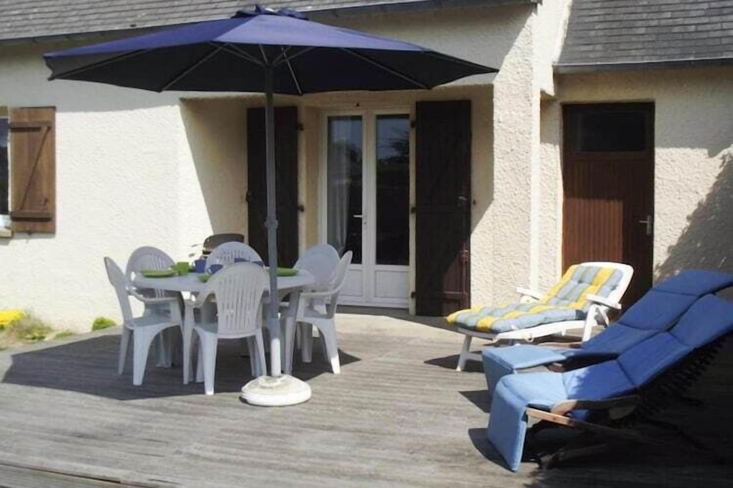 Een terras met een tafel, stoelen en lounge fauteuils, plus een blauwe parasol.