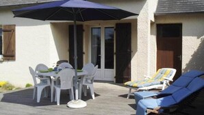 Un patio con tavolo e sedie, un ombrellone blu e poltrone da relax.
