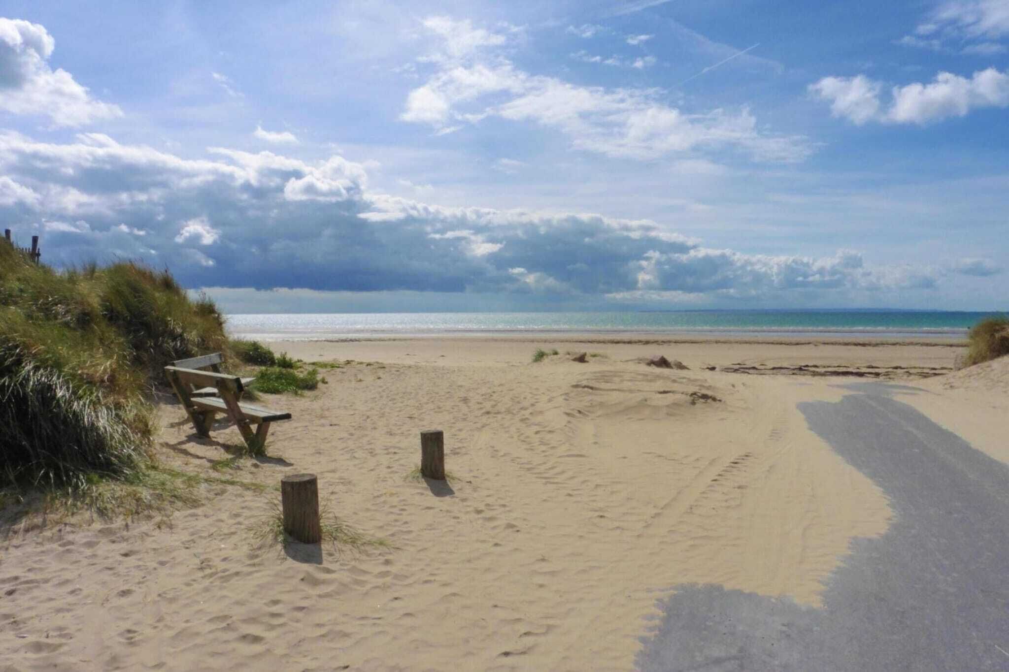 Ein Sandstrand mit einer Holzbank und einem Holzpfosten.