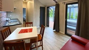 A modern room with a dining table, chairs, a red sofa, a kitchen area, and a sliding glass door leading to a balcony. - Holiday Home in Dziwnów by the Baltic Sea (Dziwnow)