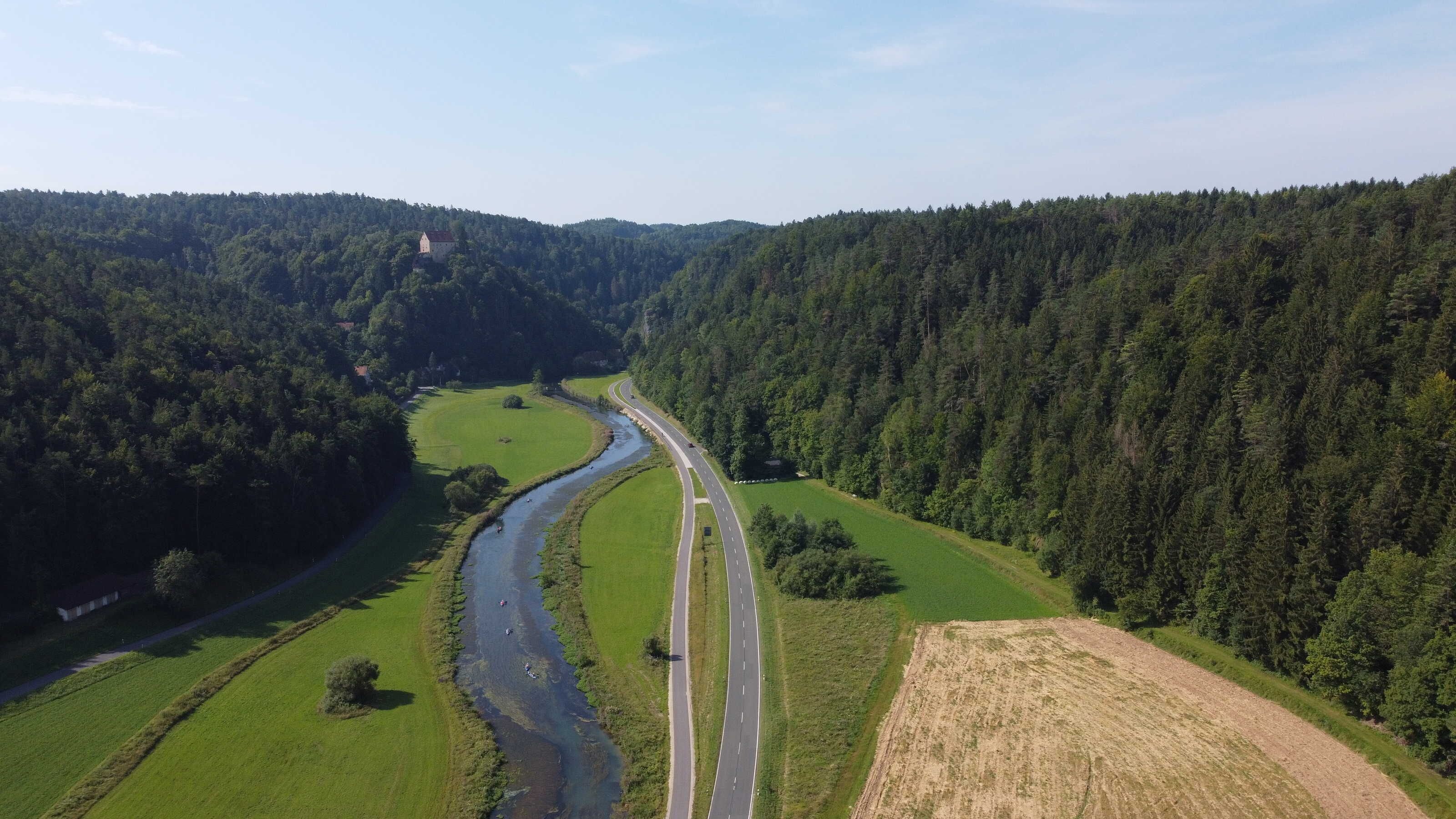 Eine gewundene Autobahn zieht sich durch ein Tal, mit einem Fluss links und dichtem Wald an beiden Seiten.