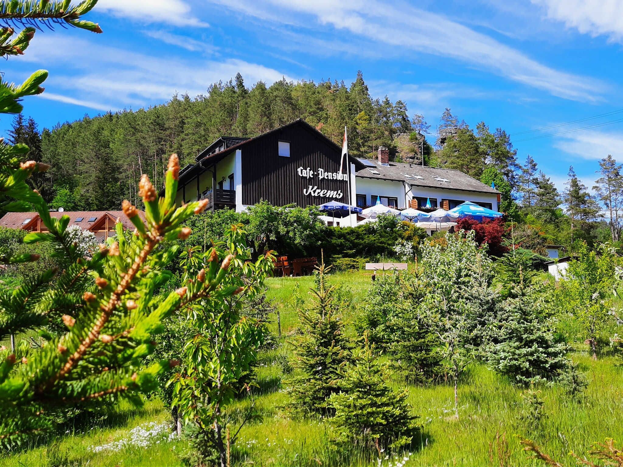 Eine Lodge mit einem großen Schild, auf dem 'Cafe Pension Kemps' steht, umgeben von üppiger Vegetation und Bäumen.