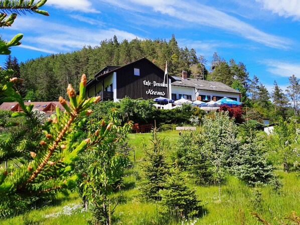 A lodge with a large sign reading 'Cafe Pension Kemps' surrounded by lush greenery and trees. - Café-Pension Krems - Double Room (Waischenfeld-Heroldsberg-Tal)