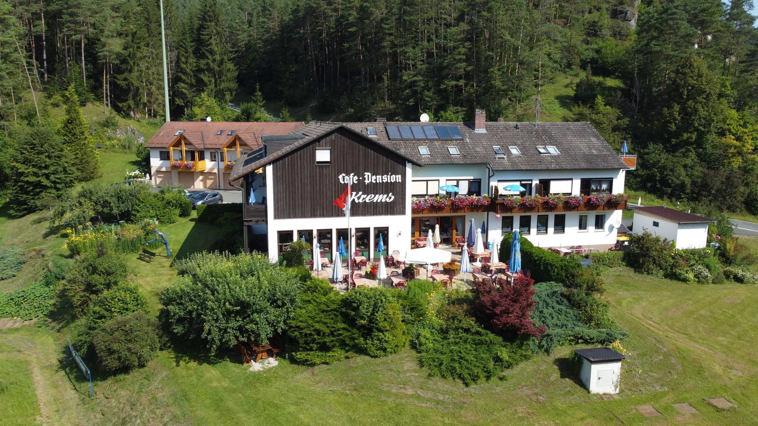 A two-story building with a cafe and pension sign, outdoor seating, and a garden area.