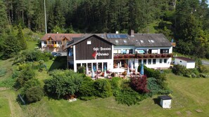 Un edificio de dos pisos con una cafetería y pensión, mesas al aire libre y un jardín.