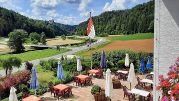 Eine Terrasse mit Sitzgelegenheiten im Freien, einer Flagge und Blick auf eine Straße und einen Wald.