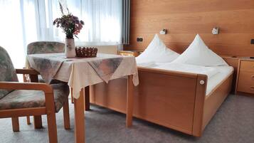 Ein Hotelzimmer mit einem Holzbett, einem kleinen Tisch mit Blumenvase, einem Sessel und einem Nachttisch.
