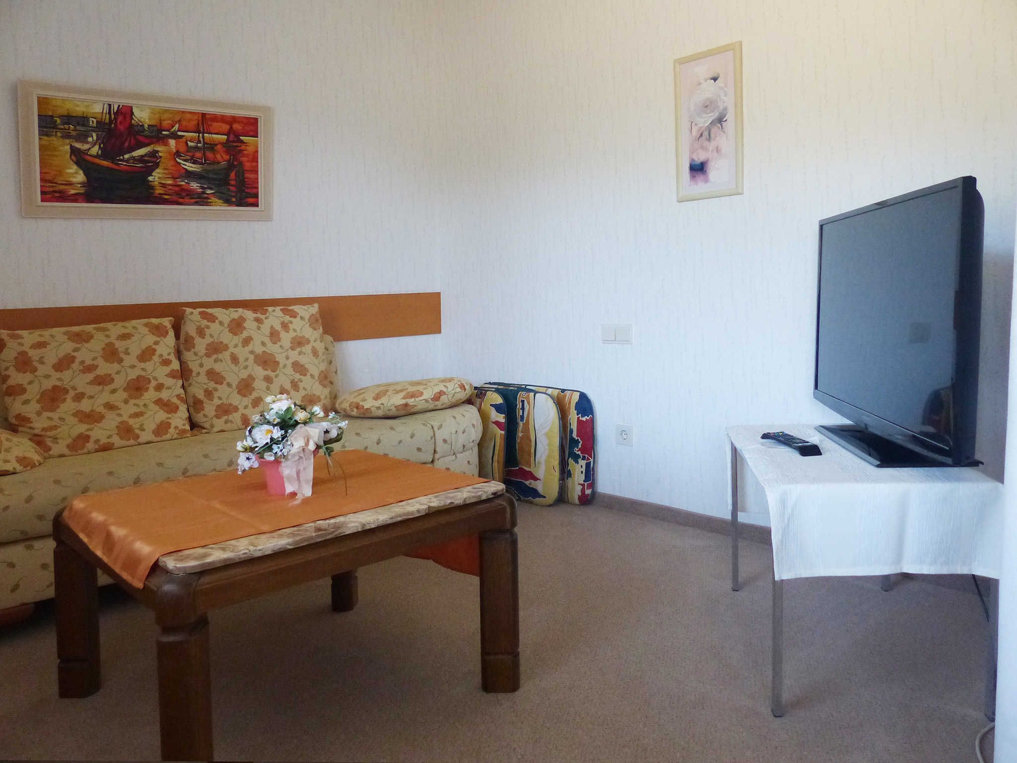 Ein Wohnzimmer mit einer Couch, einem Couchtisch, einem Fernseher und zwei Bildern an der Wand.