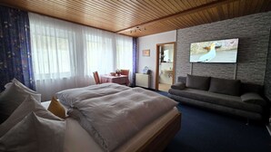 A hotel room with a wooden ceiling, a bed with pillows, a sofa, a television on the wall, and a bathroom visible through an open door. - Café-Pension Krems - Double room (Waischenfeld-Heroldsberg-Tal)