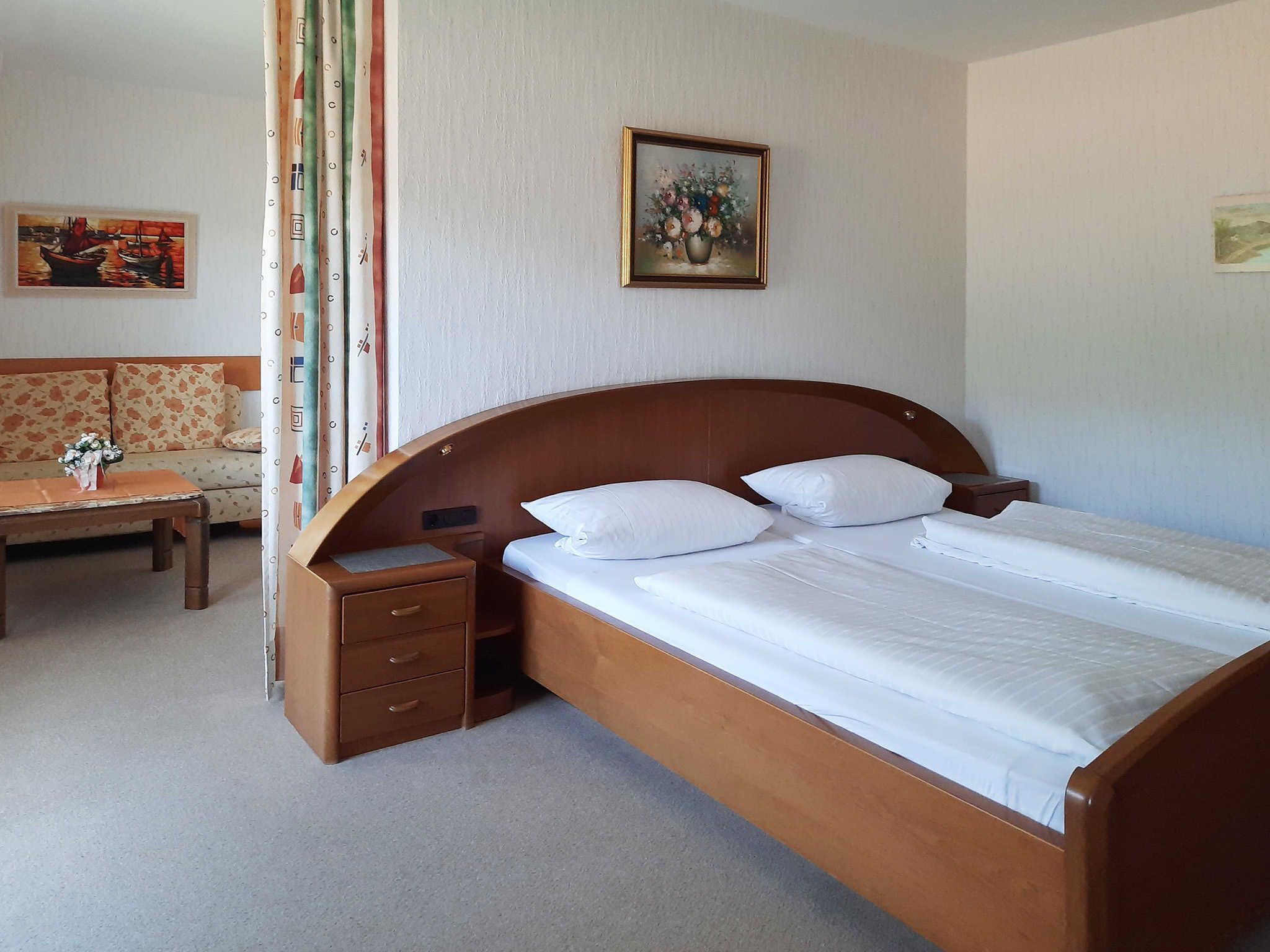 Une chambre à coucher avec un lit en bois, une table de chevet, une petite table sur laquelle est posé un vase de fleurs et un canapé.