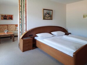 A bedroom with a wooden bed, a nightstand, a small table with a vase of flowers, and a sofa. - Café-Pension Krems - Double Room (Waischenfeld-Heroldsberg-Tal)