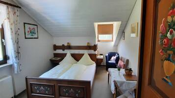 Une chambre à coucher avec un lit en bois, une petite table sur laquelle est posé un vase, une chaise et une fenêtre avec des rideaux.