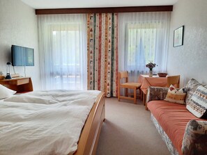 A hotel room with a bed, a sofa, a TV, a desk, and a chair. - Café-Pension Krems - Double Room (Waischenfeld-Heroldsberg-Tal)