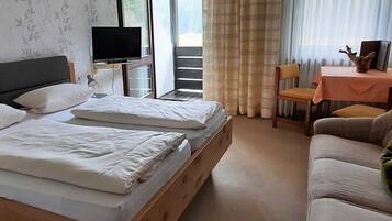 Ein Hotelzimmer mit Bett, Fernseher, Balkon, Sofa und einem Tisch mit einem dekorativen Gegenstand.