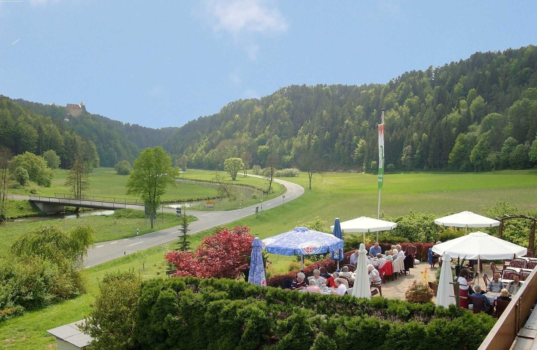Eine malerische Außenanlage mit einer Brücke, einer Straße und einer Gruppe von Personen, die unter Sonnenschirmen speisen.