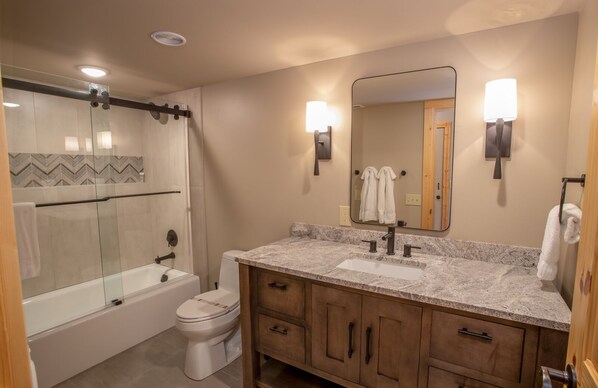 A modern bathroom with a glass shower enclosure, a bathtub, a toilet, a vanity with a sink, and a mirror.