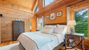 A wooden cabin bedroom with a bed, bedside table, and a window with a view of trees. - Spacious Cabin in the Mountains (Banner Elk)