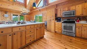 A spacious kitchen with wooden cabinets, a large island, stainless steel appliances, and a chandelier. - Spacious Cabin in the Mountains (Banner Elk)