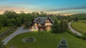 A large, two-story log cabin with a wrap-around porch, surrounded by a well-maintained lawn and dense forest. - Spacious Cabin in the Mountains (Banner Elk)