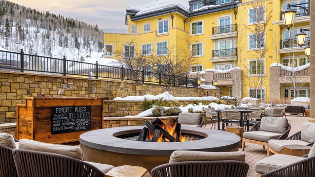 A fire pit surrounded by outdoor seating, a stone wall, and a sign with rules.