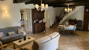 A cozy living room with a sofa, a dining table with chairs, a wooden cabinet, and a staircase leading to another level.