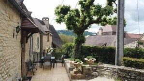 A stone building with a tiled patio, outdoor seating, and a tree.