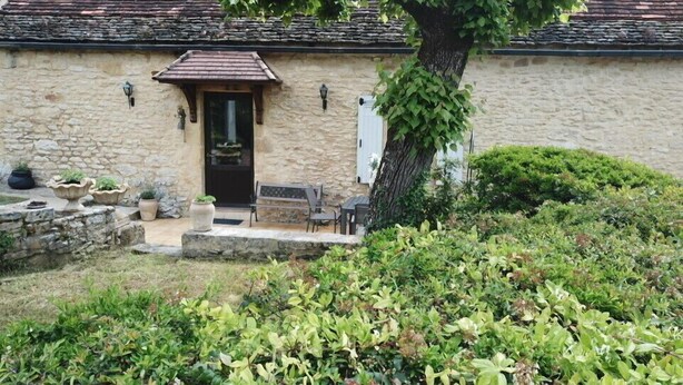 A stone building with a tiled roof, a black door, and a small porch with outdoor seating.
