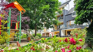 Een speelplaats met klimtoestellen en glijbanen, omringd door bomen en bloeiende planten.