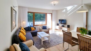 Een moderne woonkamer met een bank, salontafel, stoelen, een flatscreen televisie en een balkon met tuinmeubilair.
