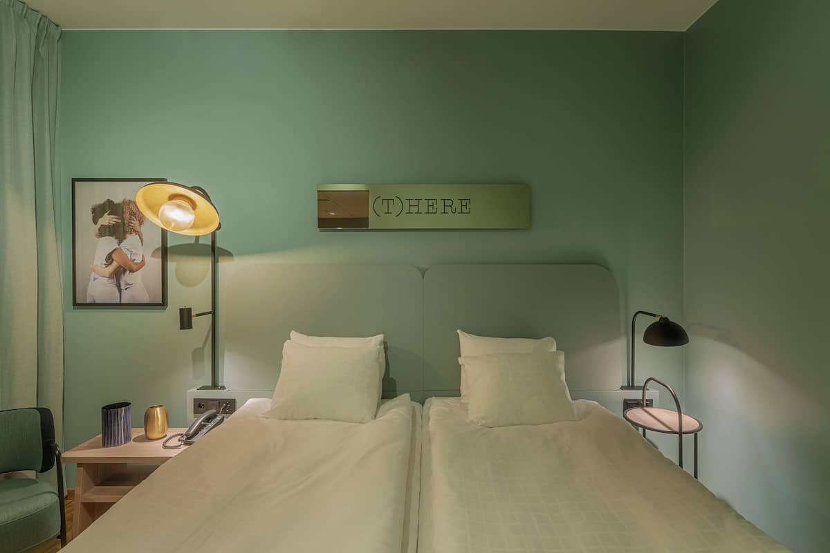 Ein Doppelbett mit weißer Bettwäsche, ein Nachttisch mit Lampe, ein gerahmtes Bild und ein Schild über dem Bett.
