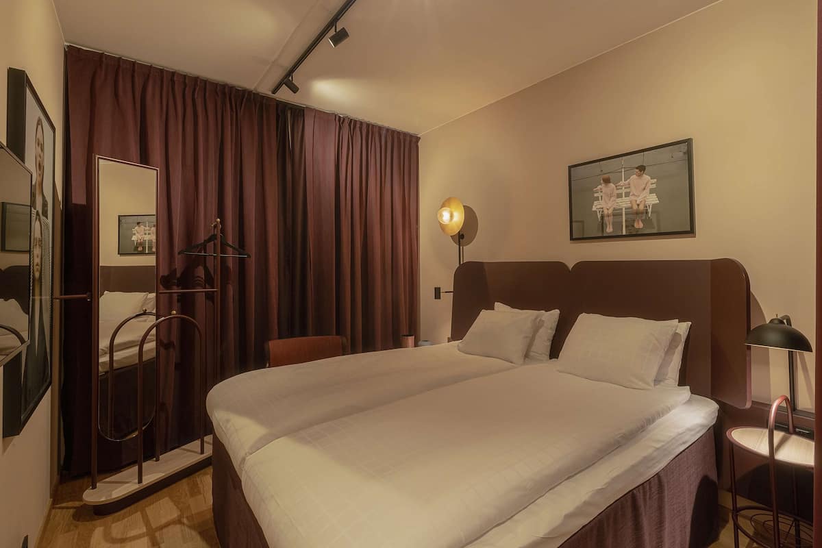 Ein Hotelzimmer mit einem großen Bett, einem Kleiderschrank, einem Spiegel, einem Schreibtisch und einer Lampe.