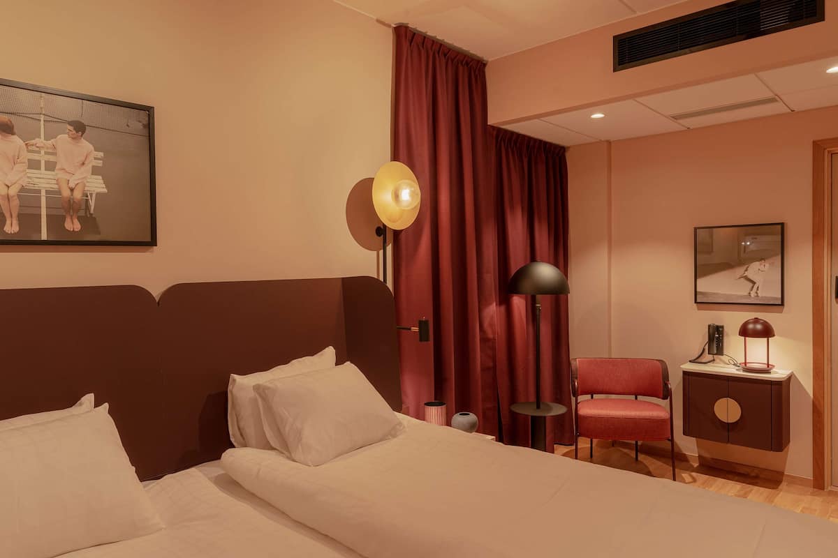 Ein Hotelzimmer mit Bett, Stuhl, Schreibtisch mit Lampe und einem Bild an der Wand.