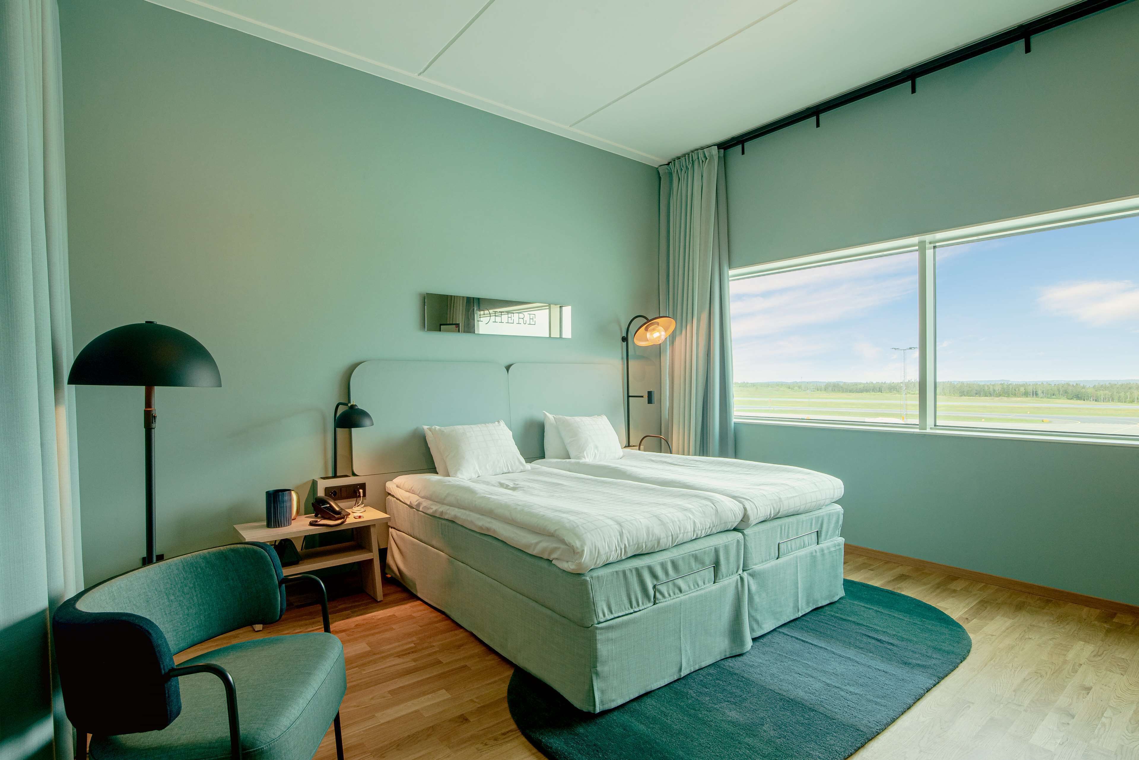 A bedroom with a bed, a desk, a chair, a lamp, and a window with a view of the outdoors.