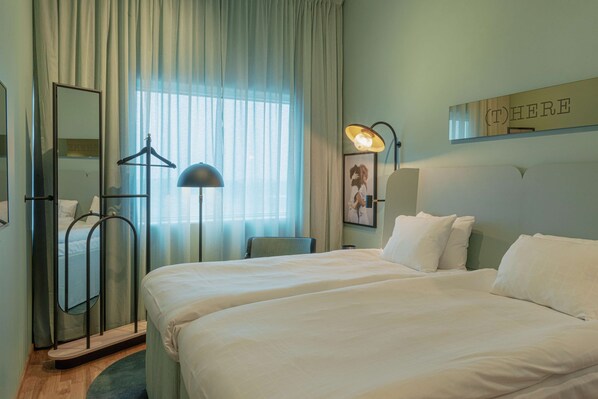Une chambre d’hôtel avec deux lits, un grand miroir, un porte-manteau mural, une lampe sur pied et un panneau accroché au mur.