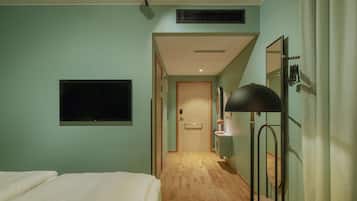 A hotel room with a bed, a TV mounted on the wall, a desk with a lamp, and a mirror.