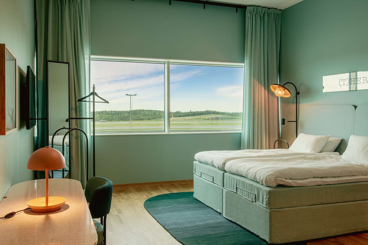 Ein Schlafzimmer mit Bett, Schreibtisch mit Lampe, Stuhl, Fenster mit Blick auf ein Feld und einem Schild an der Wand.