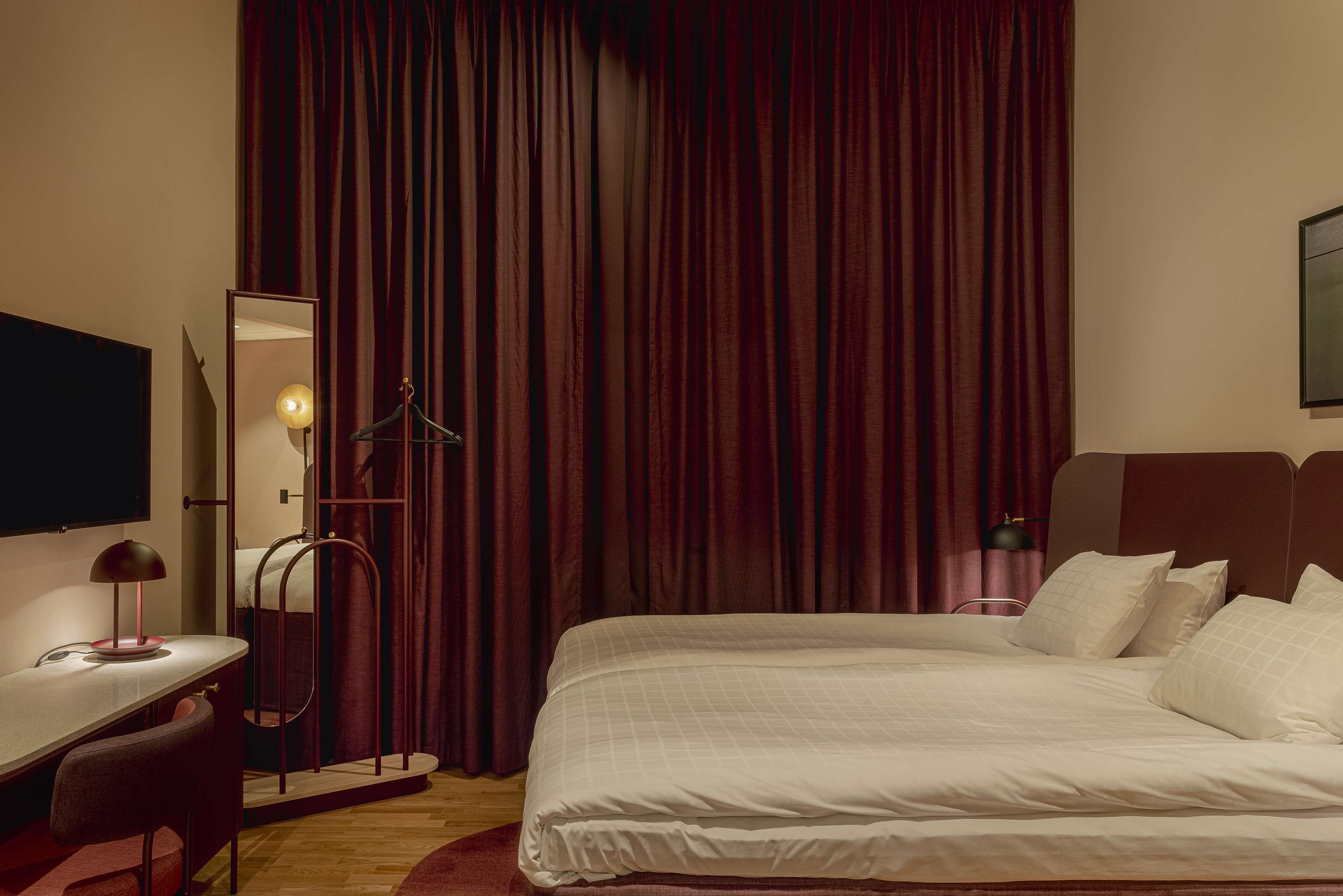 A hotel room with a bed, a desk, a chair, a mirror, and a TV.
