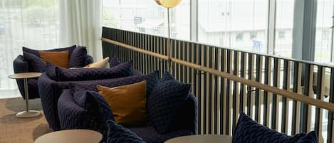 Un área de estar moderna con un sofá de color azul oscuro, mesas redondas y una lámpara de pie con forma de corazón.