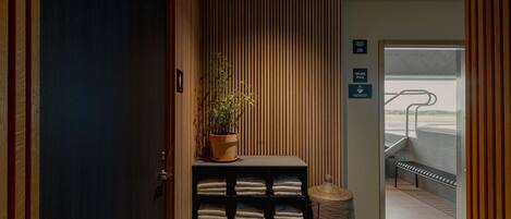 A reception area with a wooden wall, a potted plant, a shelf with folded towels, and a bench by a window.