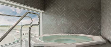A modern bathroom with a large bathtub, a view of an airport, and a herringbone-patterned wall.