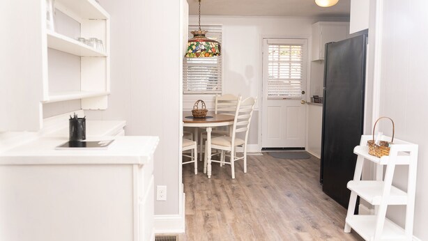 A compact kitchen with white cabinetry, a dining table with chairs, a black refrigerator, and a hanging light fixture. - In the Heart of the Sandhills (Aberdeen)
