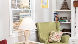 A room with a green armchair, a white table with a lamp, a bookshelf, and a window with blinds. - In the Heart of the Sandhills (Aberdeen)