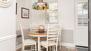 A dining area with a round table, four white chairs, a wicker basket, a stained glass pendant light, a wall clock, and a door with blinds. - In the Heart of the Sandhills (Aberdeen)
