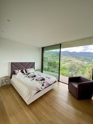 A modern bedroom with a large bed, a view of a green landscape, and a dark armchair. - Villa Individuelle Avec Piscine / Terrain, vue - Gères - Caniçada - Rio Cavado (Ventosa)