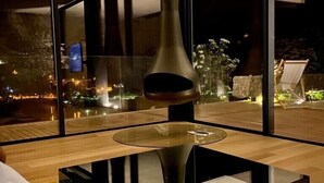 Una sala de estar moderna con una mesa de centro de vidrio, un amplio ventanal con vistas a la ciudad de noche y una lámpara de pie escultórica y original.